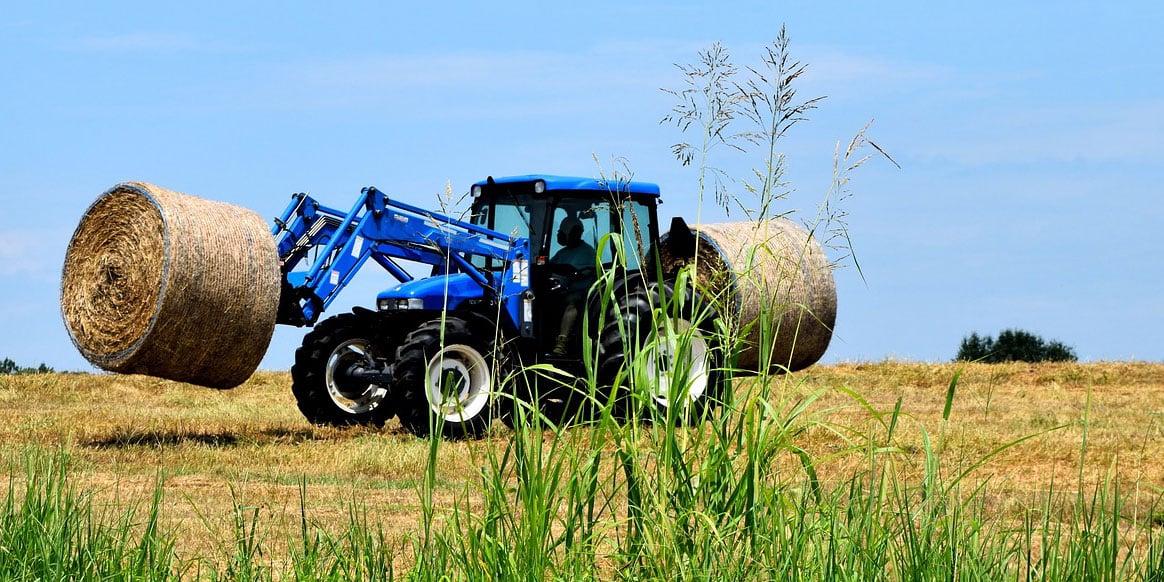 Tracteur équipé d'un chargeur frontal soulevant une balle ronde de foin